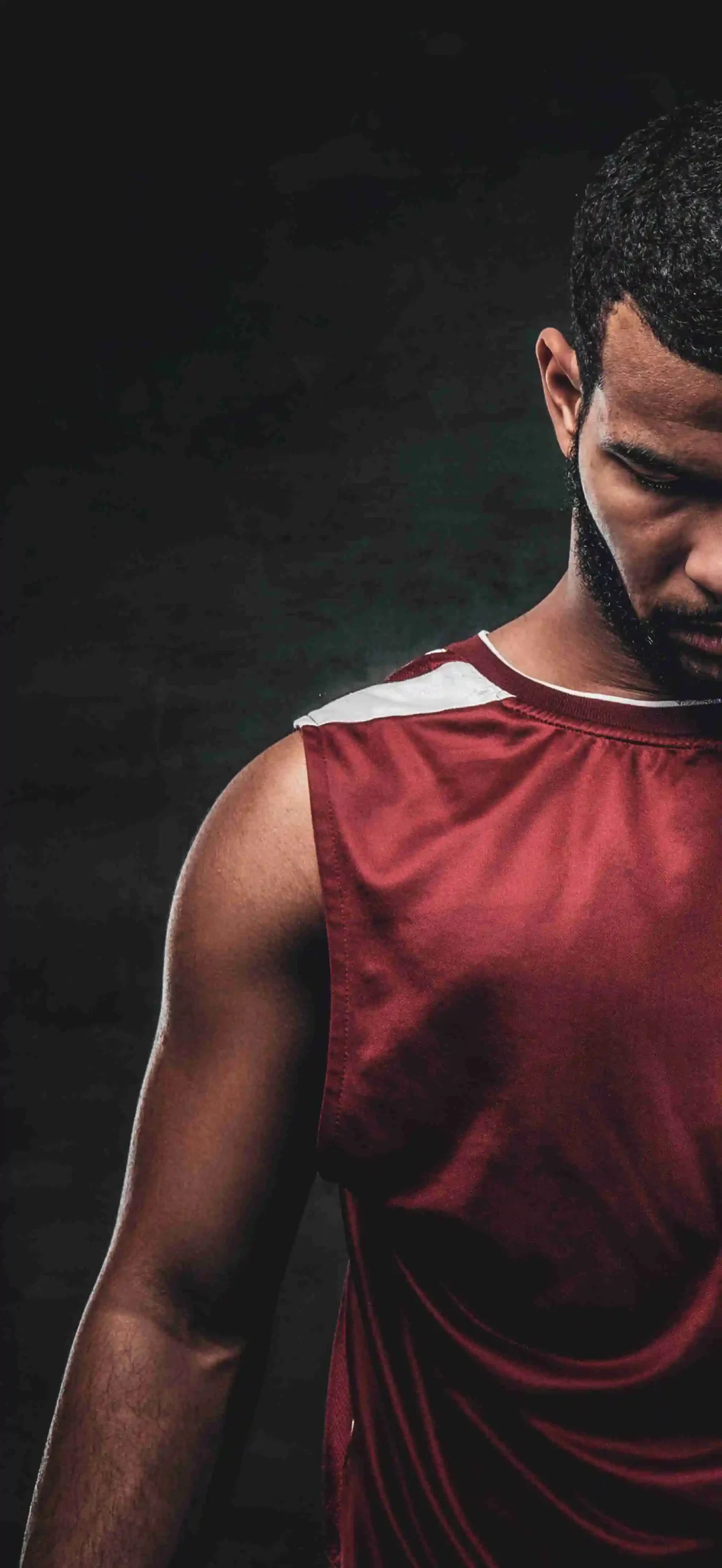 Athlete in a dark red jersey standing in deep mental focus and composure against a dark background