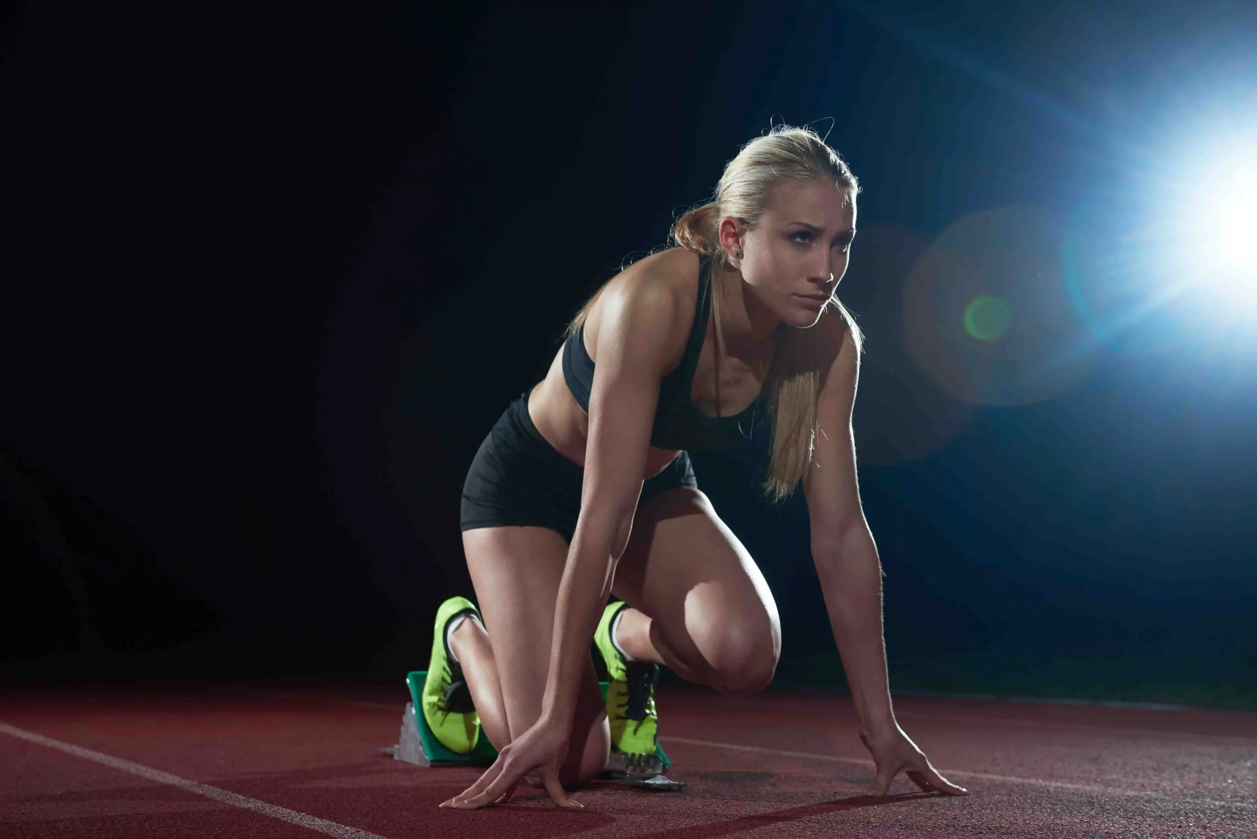 Focused athlete in starting blocks on a dark track preparing mentally and physically before a sprint